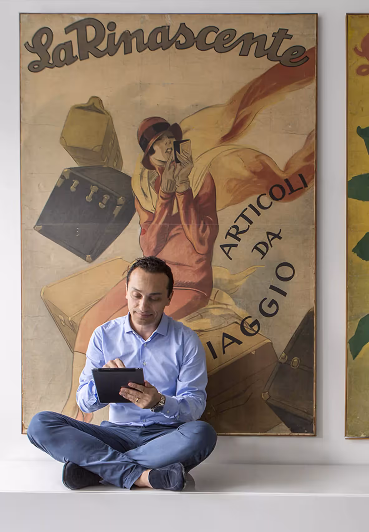 Un dipendente lavora al tablet seduto davanti a un manifesto storico de La Rinascente